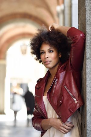 Woman standing in archway in red leather jacket and hand in hair