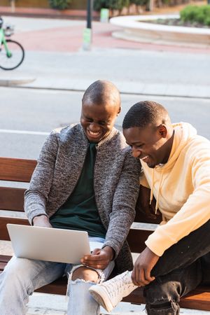 Smiling Black men using laptop while sitting on bench