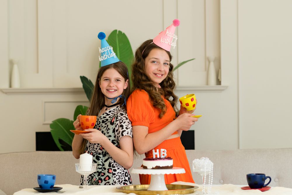 Two girls back-to-back in birthday hats