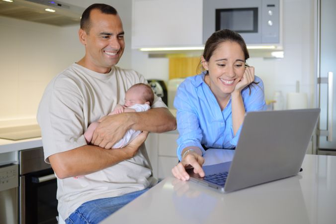 A man and woman holding a baby in front of a laptop