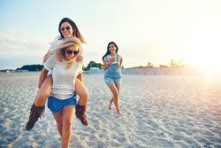 Three joyful female friends having fun walking on sand at the beach
