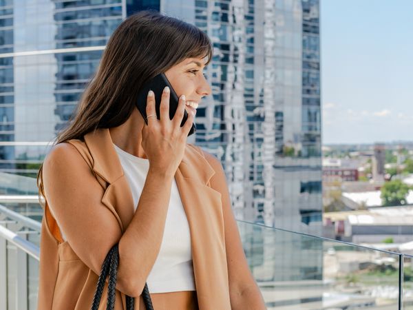Side view of a businesswoman standing on her office balcony and talking on her cell phone during her office break.