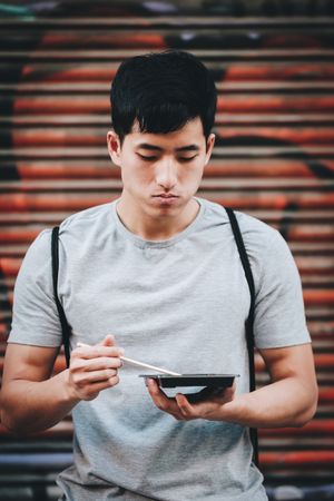 Asian man eating takeaway food with chopsticks on city street