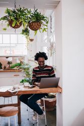 Man smiling while working on his computer at a coffee shop with hangplants