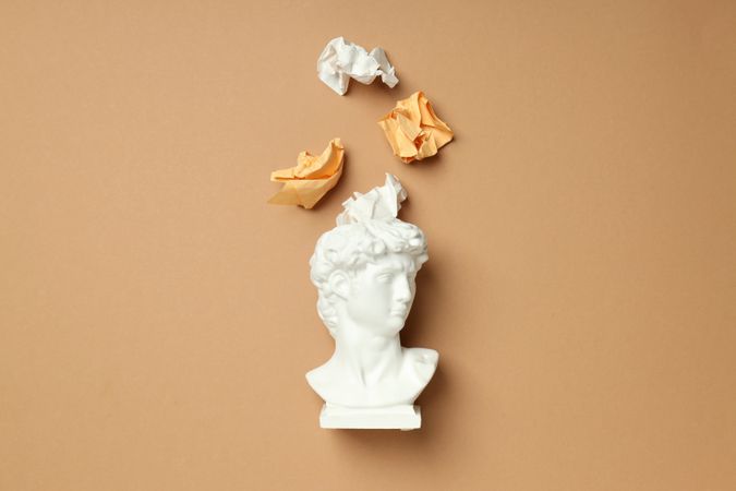 Marble bust with crumpled paper coming out of brain on brown background