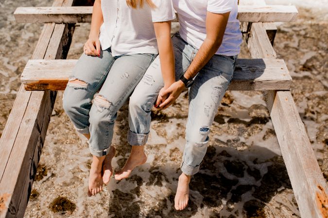 Glad lovers sitting on destroyed pier on seashore