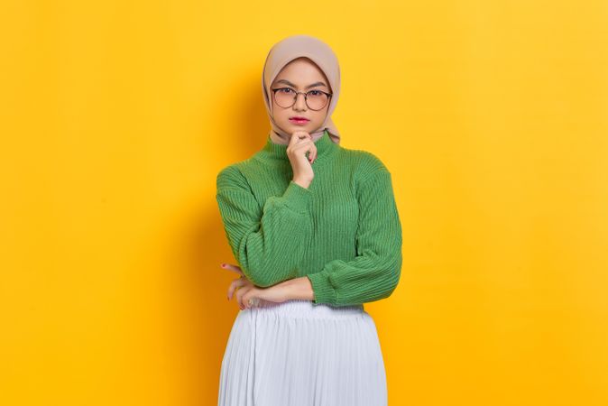 Woman in headscarf and glasses looking at camera with hand on chin