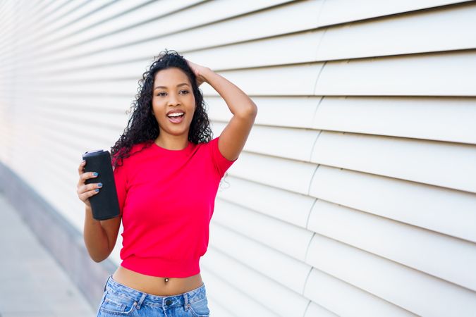 A Joyful Young Woman Posing Happily with Her Phone Against a Vibrant Modern Background