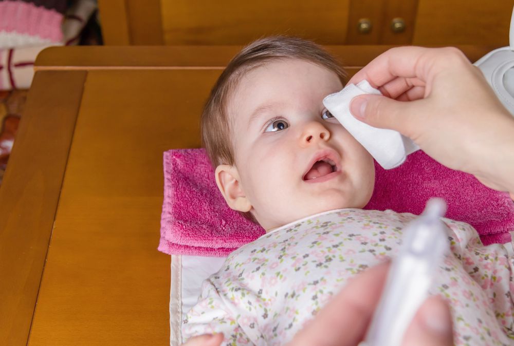 Mother cleaning baby's eyes with cotton