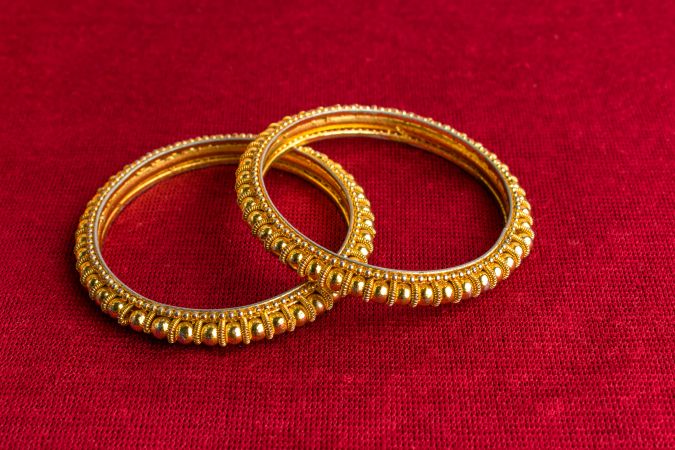 Beautiful shiny golden bangles with Indian traditional design on a red velvet background