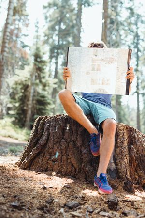 young man holding map and checking for road sitting on the woods