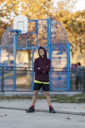 Portrait of smiling boy in hooded shirt standing in basketball court in autumn