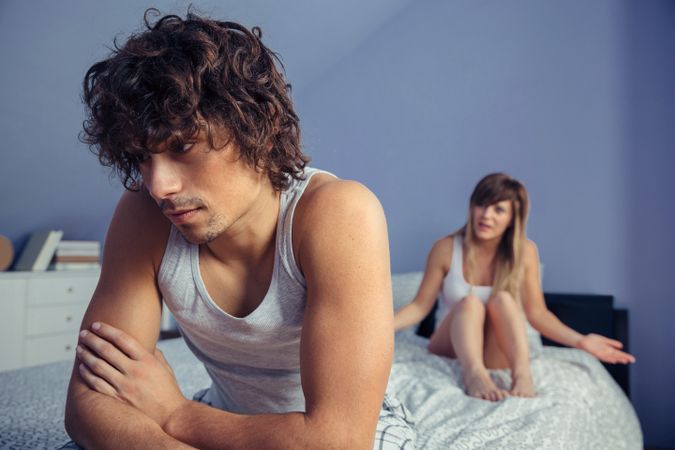 Man sitting over bed listening to woman during quarrel
