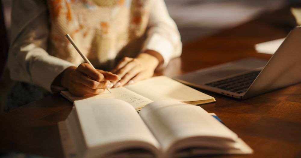 Anonymous Woman Writing Notes From Textbooks and Laptop for College Project.