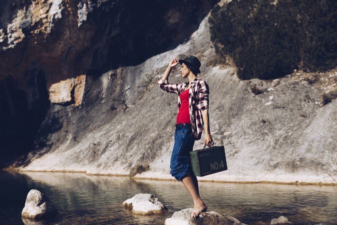 woman standing on rock with case near clear water in lake