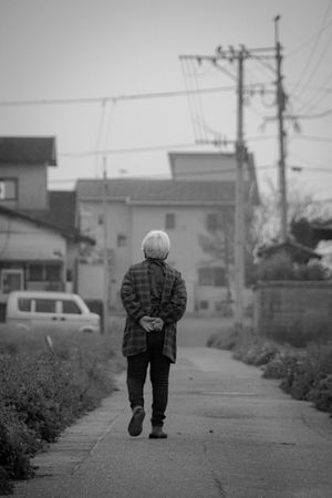 Backside of an older man walking outdoor in grayscale