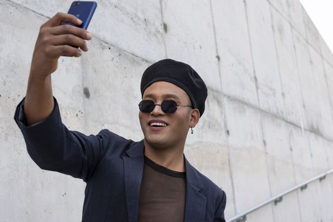 Young Latino gay man with make-up on wearing a fashionable hat and sunglasses, taking selfies