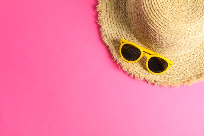 Straw hat with sunglasses on color background, space for text, top view. Summer backdrop