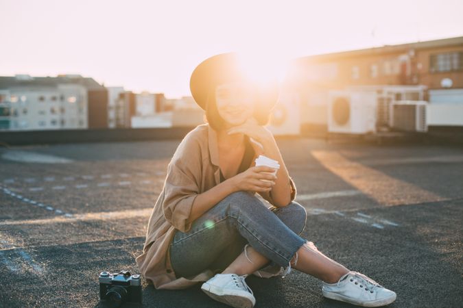 Woman in trendy clothes on rooftop with to-go beverage