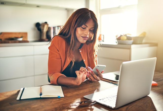 Businesswoman texting while working at her kitchen table