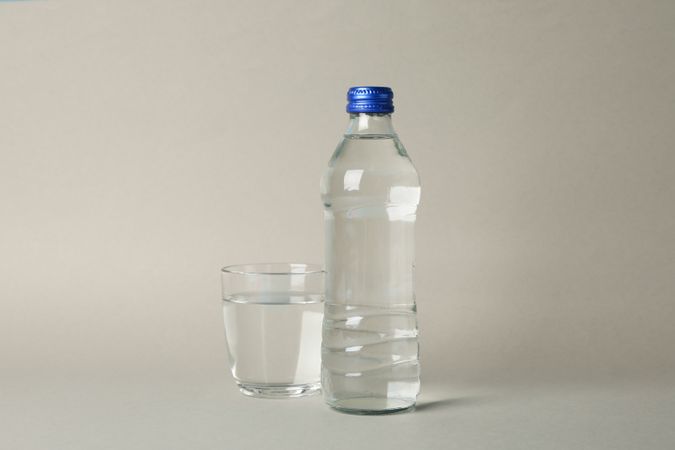 Plastic water bottle with glass in beige room with copy space