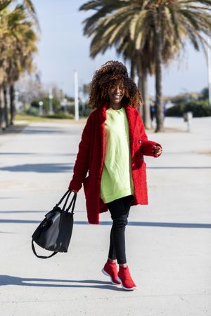 Smiling female with curly hair walking on palm tree lined street