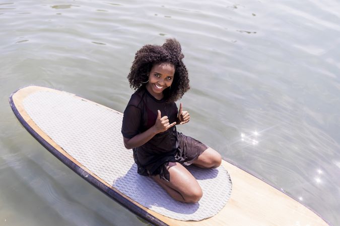 Young Black woman sitting on paddle board in the water
