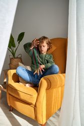Boy stretching colorful strings in armchair