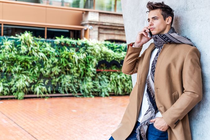 Man in camel coat and scarf standing outside with phone to his ear