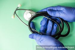 Looking down at green table with hands in blue latex gloves holding stethoscope 56GWxP