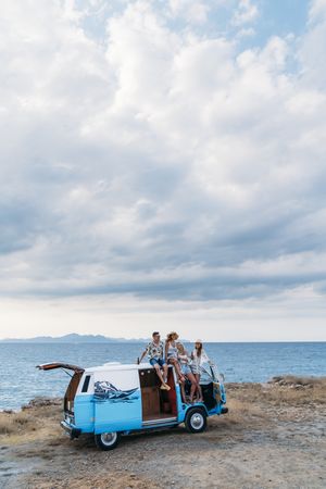 Relaxed friends comfortable placing on top of blue car