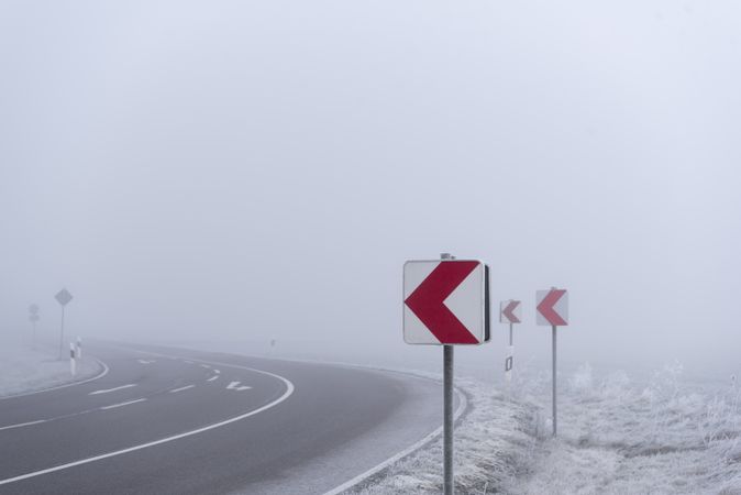 Warning road signs before dangerous curve in dense mist