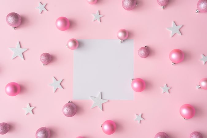 Different shades of pink baubles and stars on a pink background with paper card