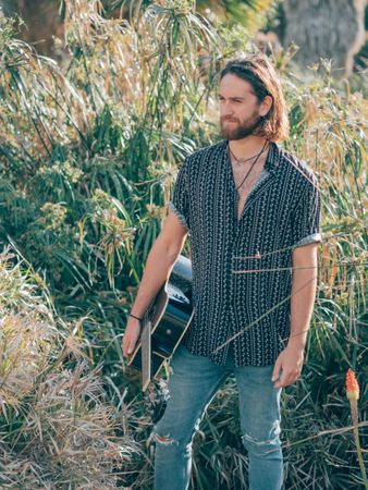 Hipster man in jungle with guitar