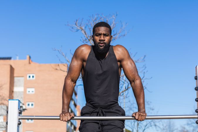 Strong Black sportsman working out on bar in town