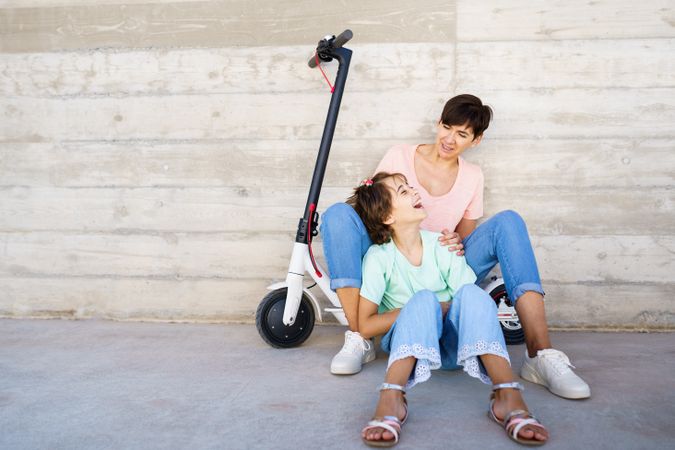 Woman and preteen girl outside talking together with a scooter with copy space