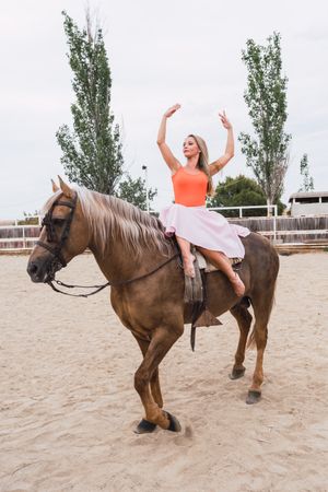 Graceful rider sitting at harnessed horse walking along paddock