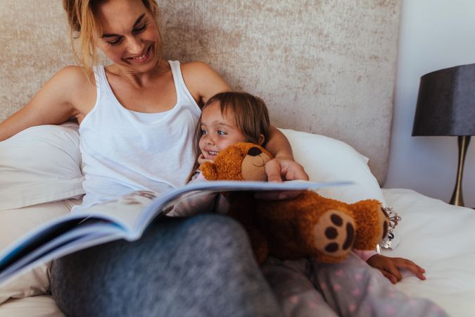 Woman looking at her daughter and smiling while reading a book in bedroom