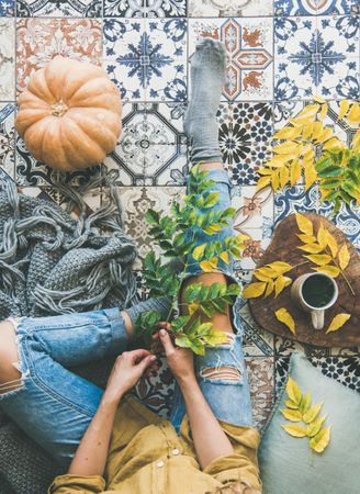Woman sitting on colorfully tiled balcony with fall leaves, squash, and mug, vertical composition