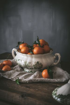 Orange tangerines in ceramic ornamental bowl on wooden table