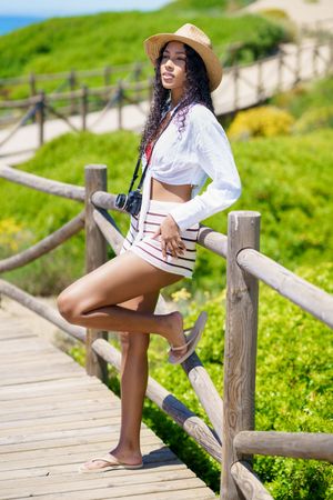 A Stylish Young Woman Dressed in Resort Attire Stands Gracefully on a Beautiful Scenic Pathway