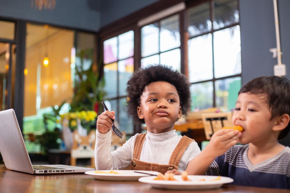 Two children snacking in a cafe with laptop