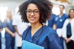 Portrait of smiling Black woman in scrubs and stethoscope, holding documents