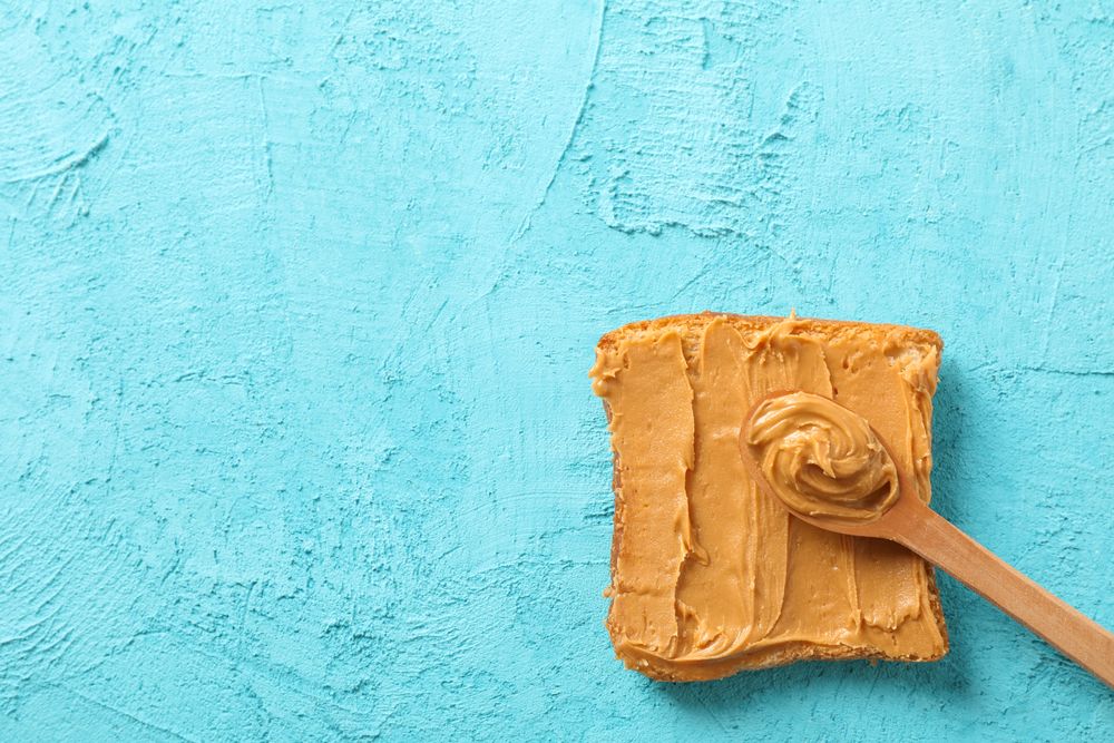 Peanut butter sandwich and spoon on color background, space for text and top view