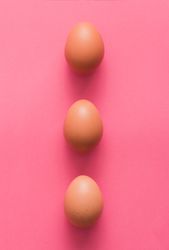 Row of three brown Easter eggs on pink background