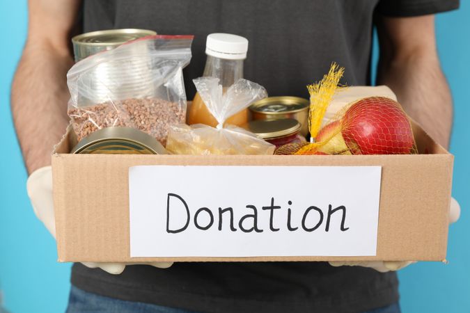 Young man holds donation box against blue background. Volunteer