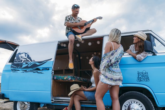 Man playing on guitar on car roof and women listening with pleasure