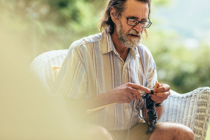 Man with beard sitting on chair and knitting