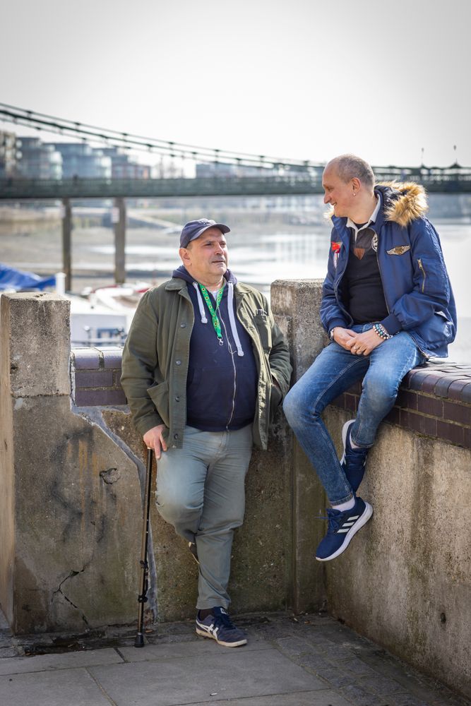 Two male friends sitting by the river and talking, vertical