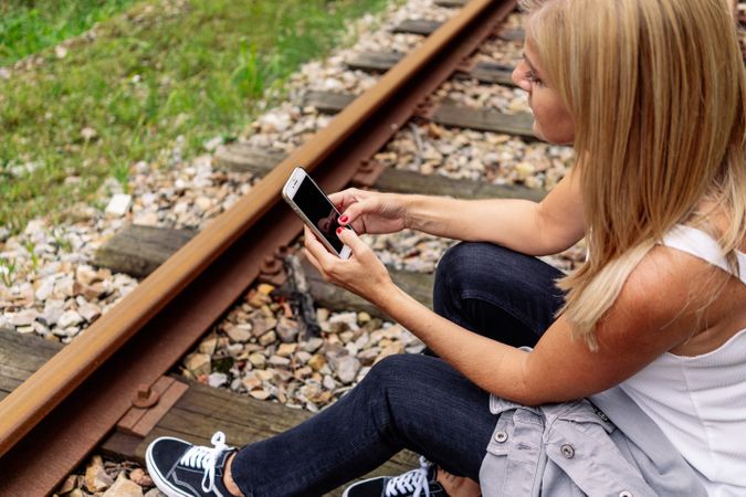 Cheerful woman sitting on railway with smartphone